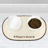 A beige microfibre pet bowl mat with a brown paw print design, personalised with the name 'Pippa', alongside two white bowls filled with pet food.