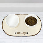 A beige microfibre pet bowl mat with a brown paw print design, personalised with the name 'Pippa', alongside two white bowls filled with pet food.