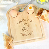 A wooden egg & toast board with a chick design and personalized text 'Isabella's Dippy Eggs' displayed, accompanied by a half-eaten egg and toast on the side.