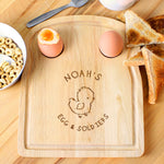 A wooden egg & toast board with a chick design and personalized text 'Isabella's Dippy Eggs' displayed, accompanied by a half-eaten egg and toast on the side.