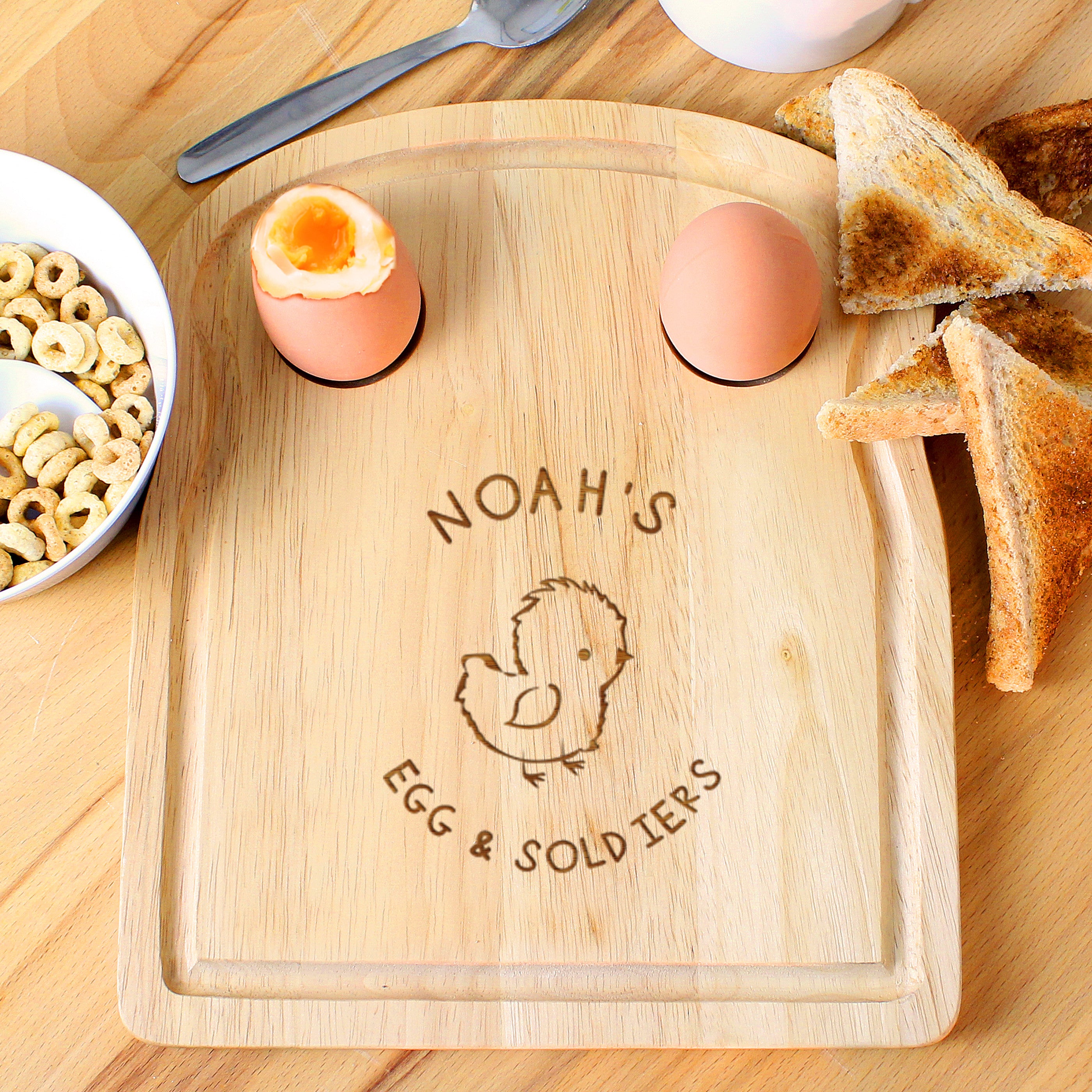 A wooden egg & toast board with a chick design and personalized text 'Isabella's Dippy Eggs' displayed, accompanied by a half-eaten egg and toast on the side.