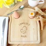 A wooden egg & toast board with a chick design and personalized text 'Isabella's Dippy Eggs' displayed, accompanied by a half-eaten egg and toast on the side.