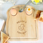 A wooden egg & toast board with a chick design and personalized text 'Isabella's Dippy Eggs' displayed, accompanied by a half-eaten egg and toast on the side.
