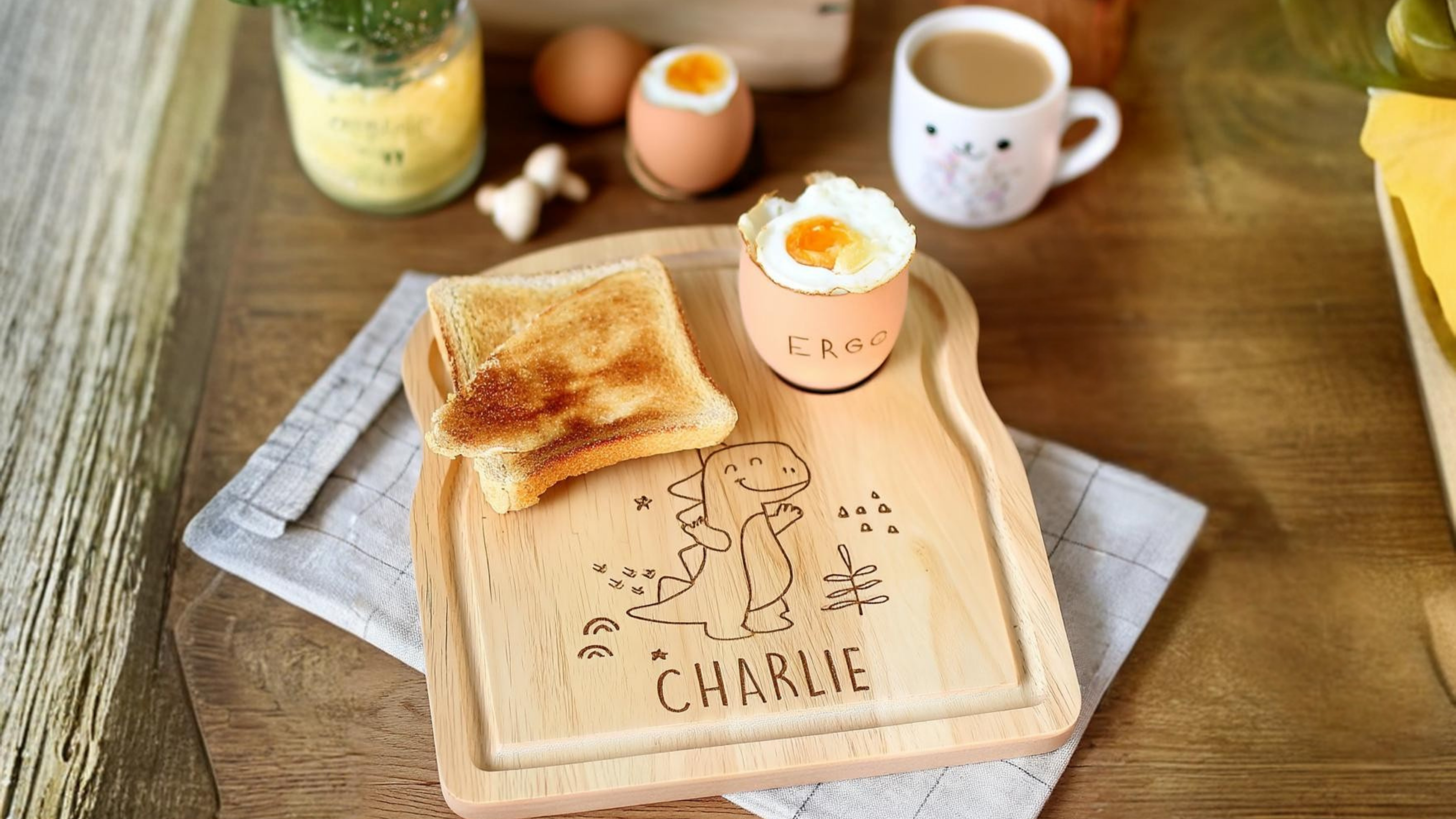 Personalised Dinosaur Egg & Toast Board Wooden tray with toast and a boiled egg on a wooden table, featuring the name 'Charlie'.