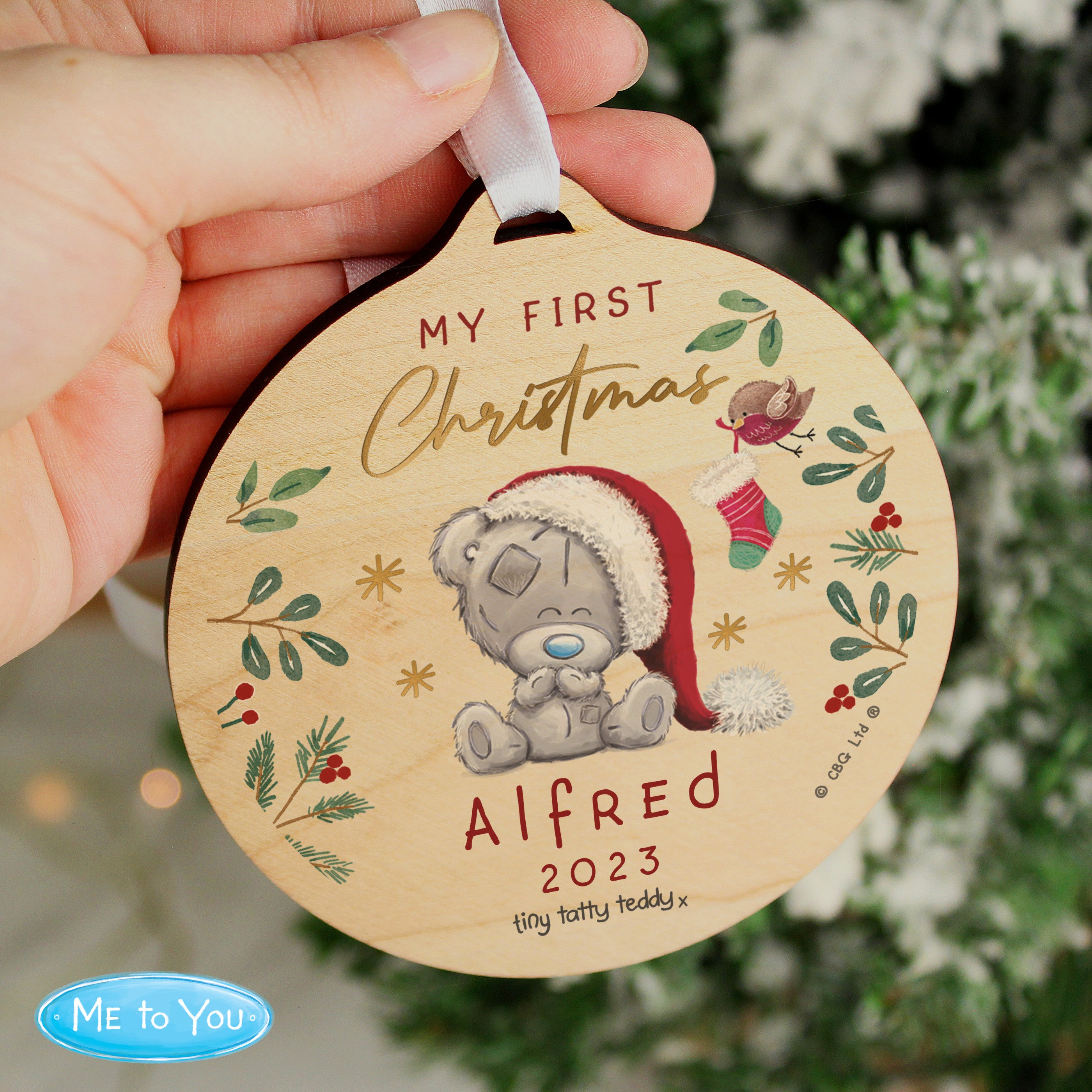 A round wooden decoration featuring an illustration of a teddy bear with a Santa hat, surrounded by Christmas-themed elements like stars, berries, and the text 'My First Christmas'. 02