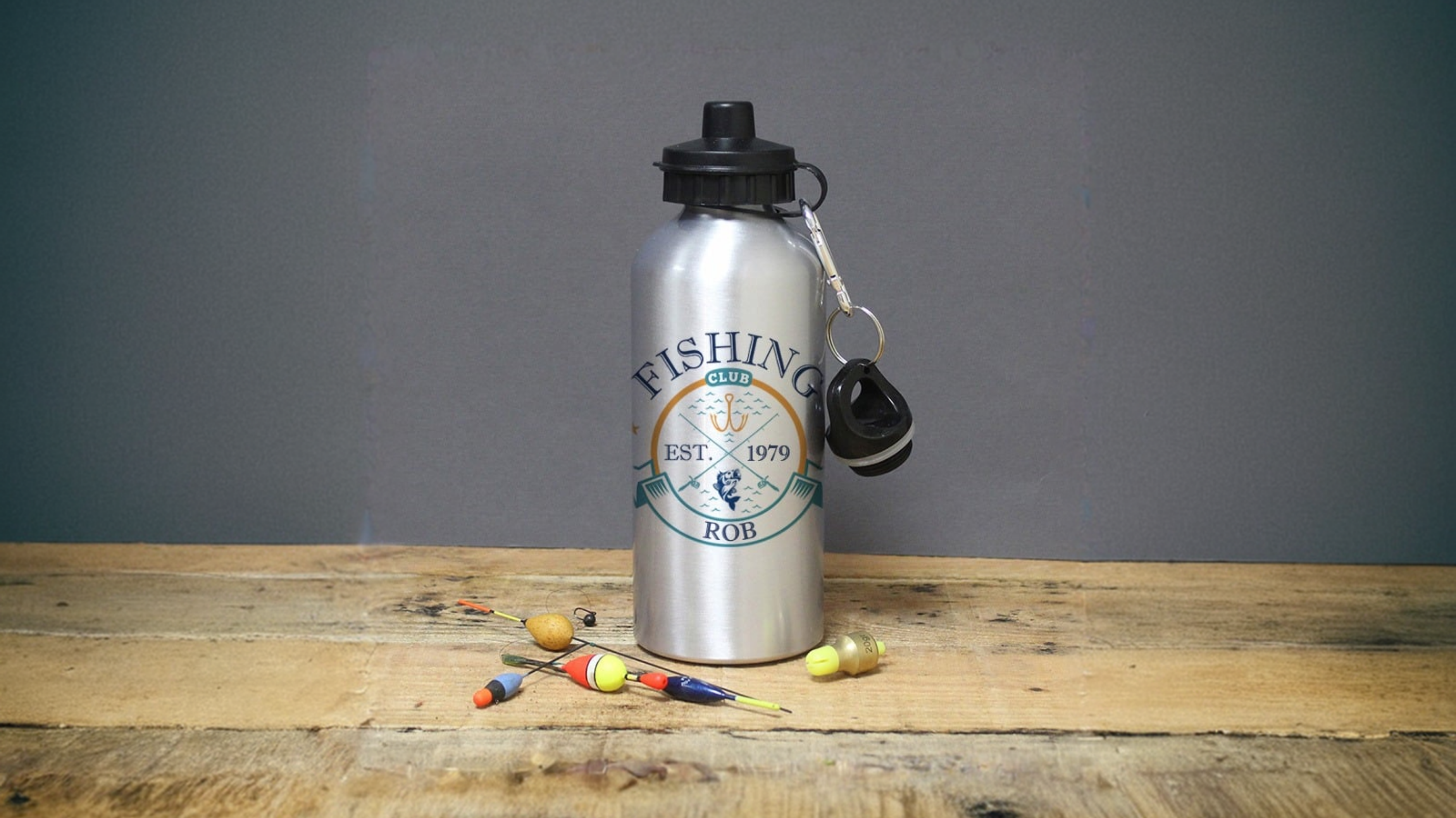 Personalised Fishing Club Silver Drinks Bottle with a label on a wooden surface against a grey background