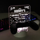 Personalised gaming controller holder with LED colour changing light, displaying a name and gaming-related phrases on a illuminated panel.