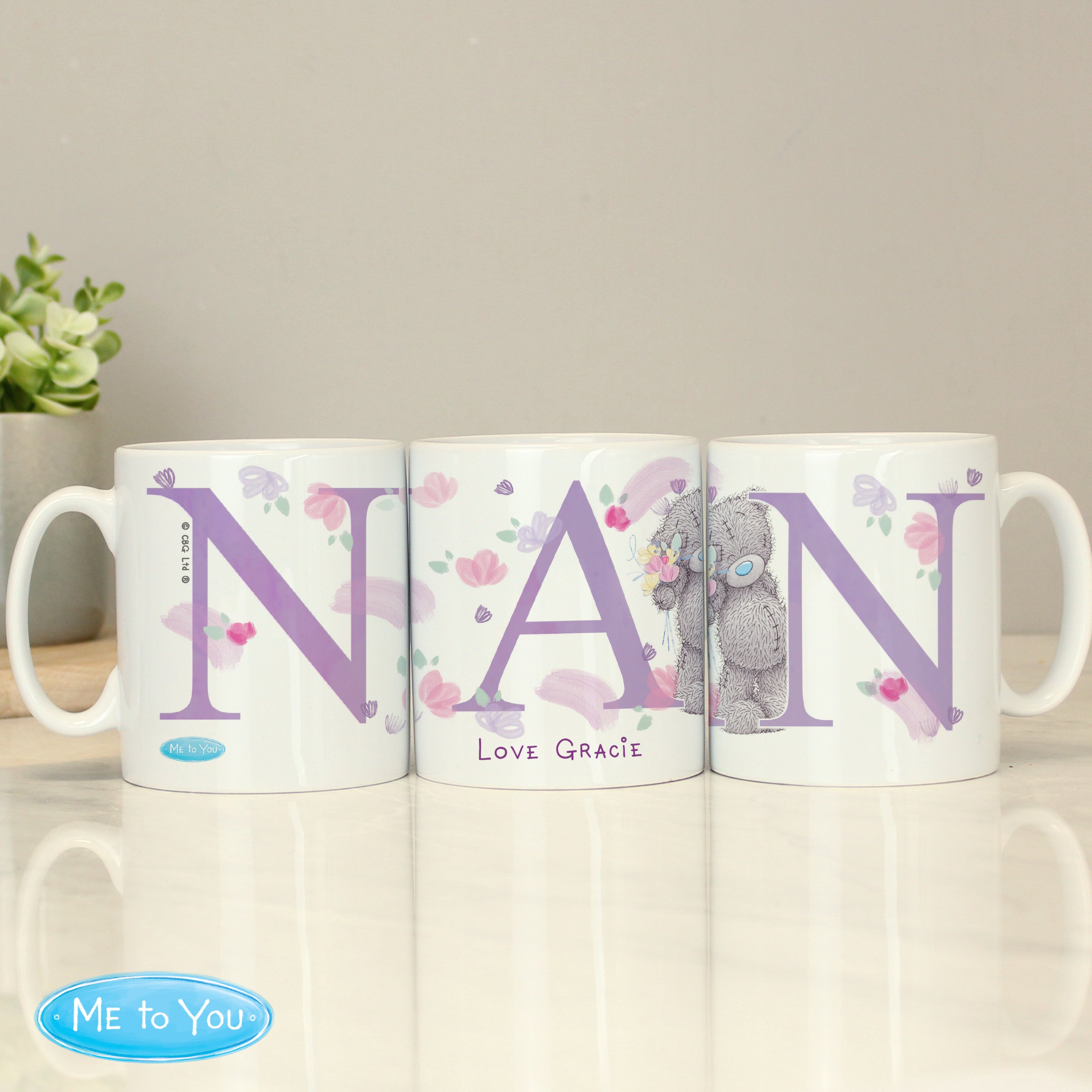 Three ceramic mugs with 'Nan' written on each, featuring floral and animal designs, placed on a table with a 'Me To You' logo in the corner.