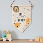 A beige-coloured hanging banner with a safari animal theme, including a lion, giraffe, and monkey, with the text 'OLIE you are so loved' displayed. 01