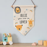 A beige-coloured hanging banner with a safari animal theme, including a lion, giraffe, and monkey, with the text 'OLIE you are so loved' displayed. 01