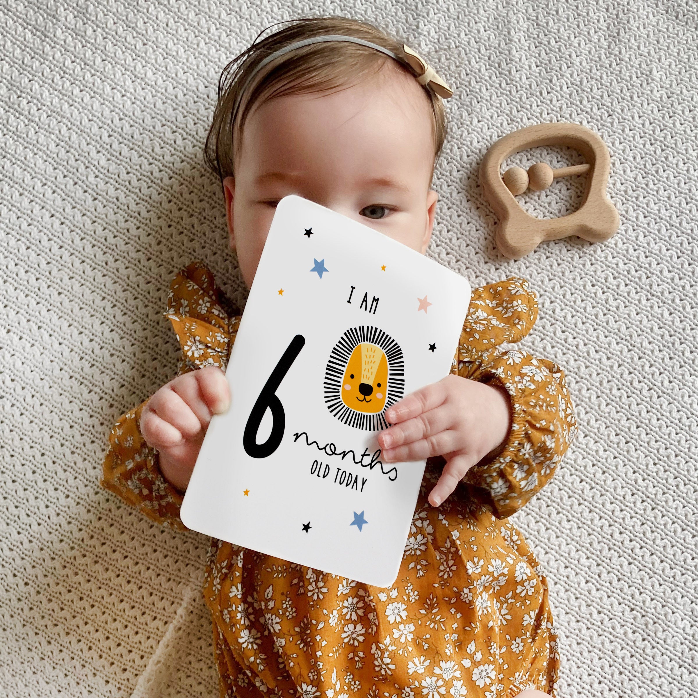 A set of personalised milestone cards with safari animal illustrations, a drawstring bag, and a small wooden clip, all laid out on a grey fabric background.
