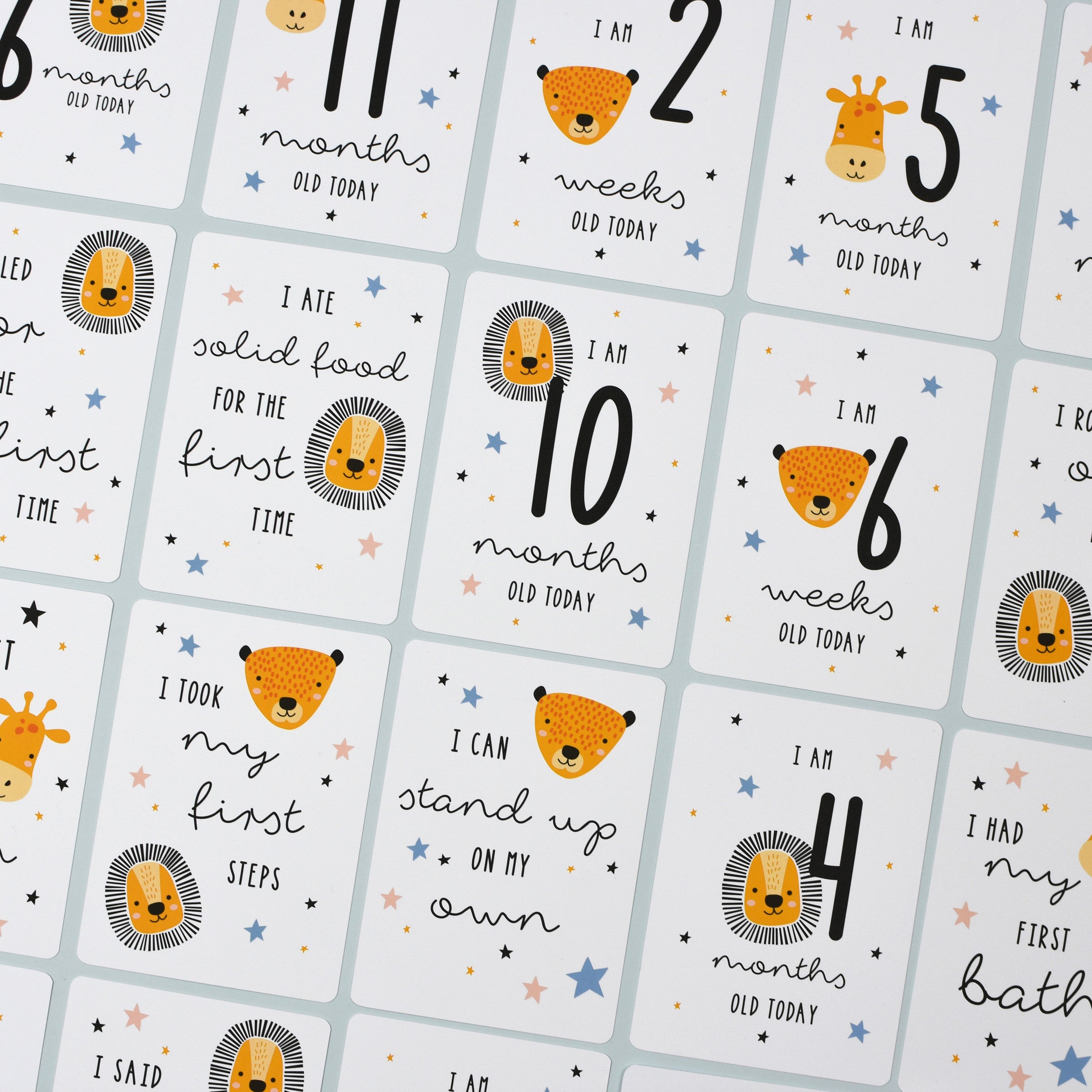 A set of personalised milestone cards with safari animal illustrations, a drawstring bag, and a small wooden clip, all laid out on a grey fabric background.