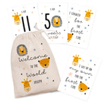 A set of personalised milestone cards with safari animal illustrations, a drawstring bag, and a small wooden clip, all laid out on a grey fabric background.