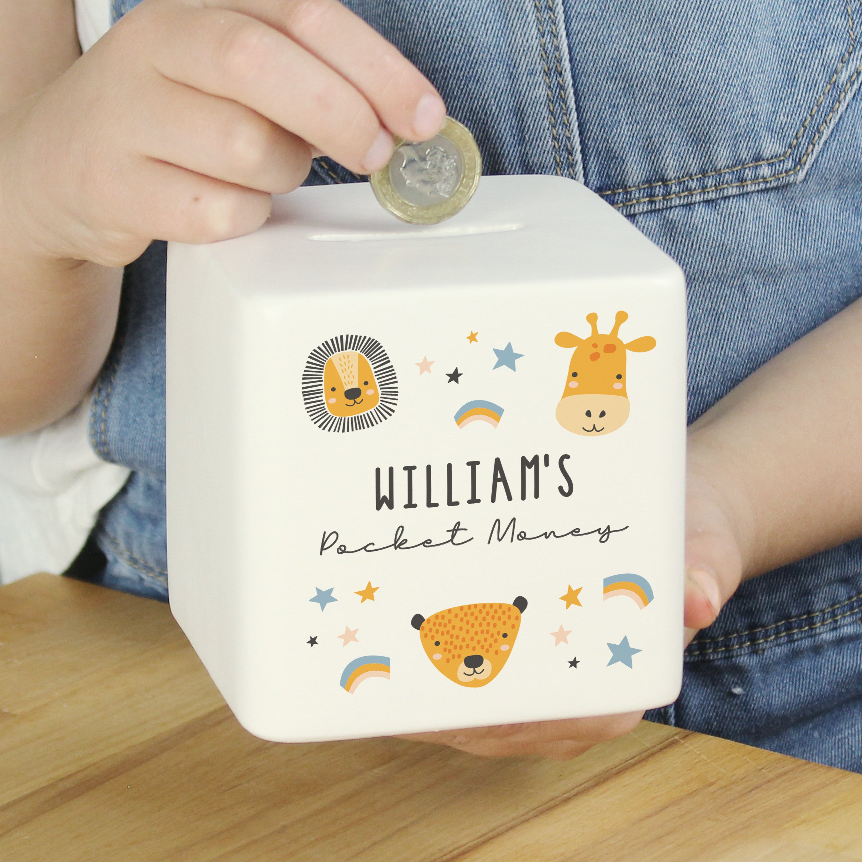 A white ceramic square money box with a personalised inscription and decorated with safari animal illustrations, including a lion and a giraffe, and the name 'Noah'.
