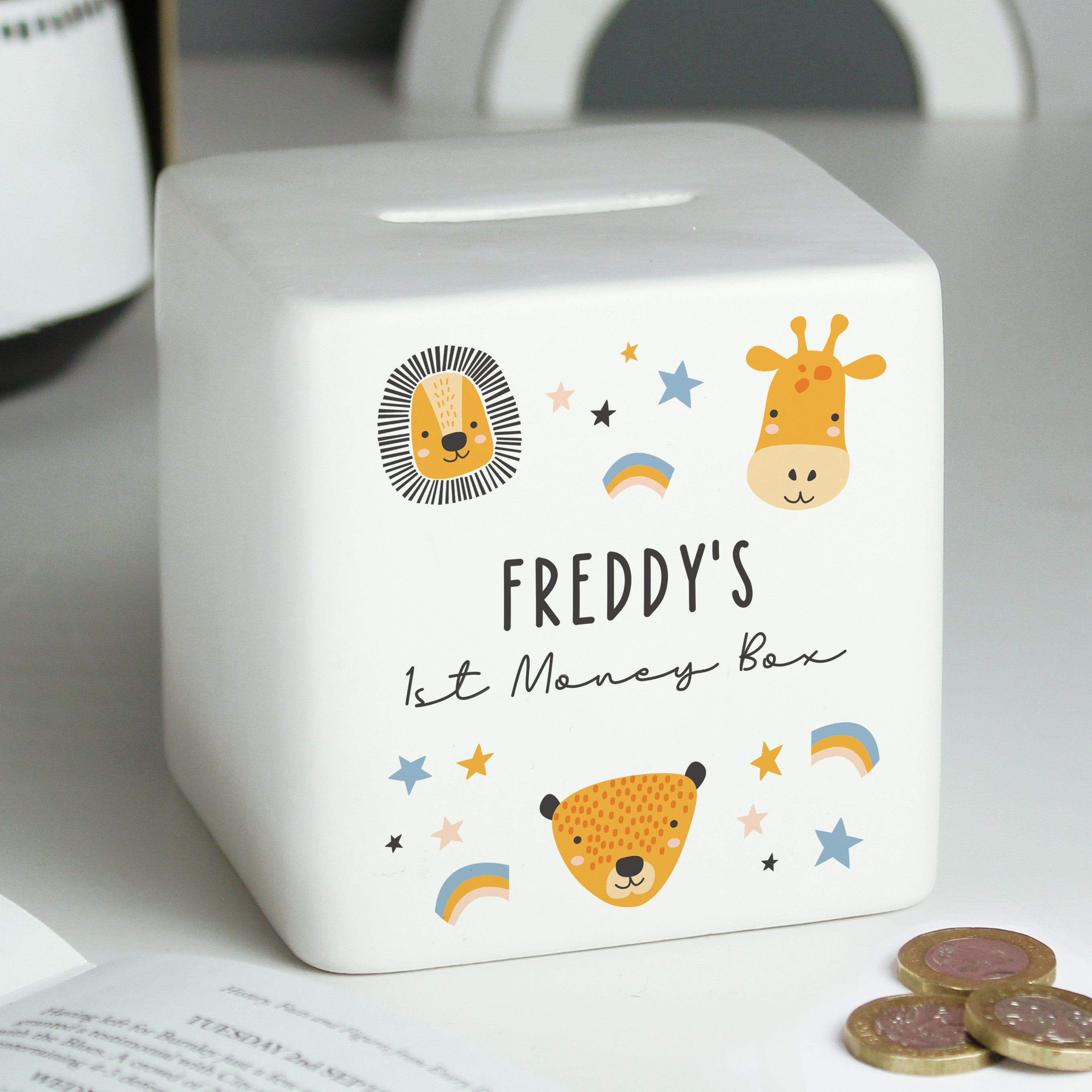 A white ceramic square money box with a personalised inscription and decorated with safari animal illustrations, including a lion and a giraffe, and the name 'Noah'.