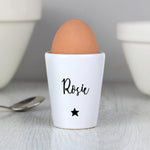 A white ceramic egg cup with the name 'Stanley' printed on it, alongside a spoon and a piece of toast, with an egg placed in the egg cup.