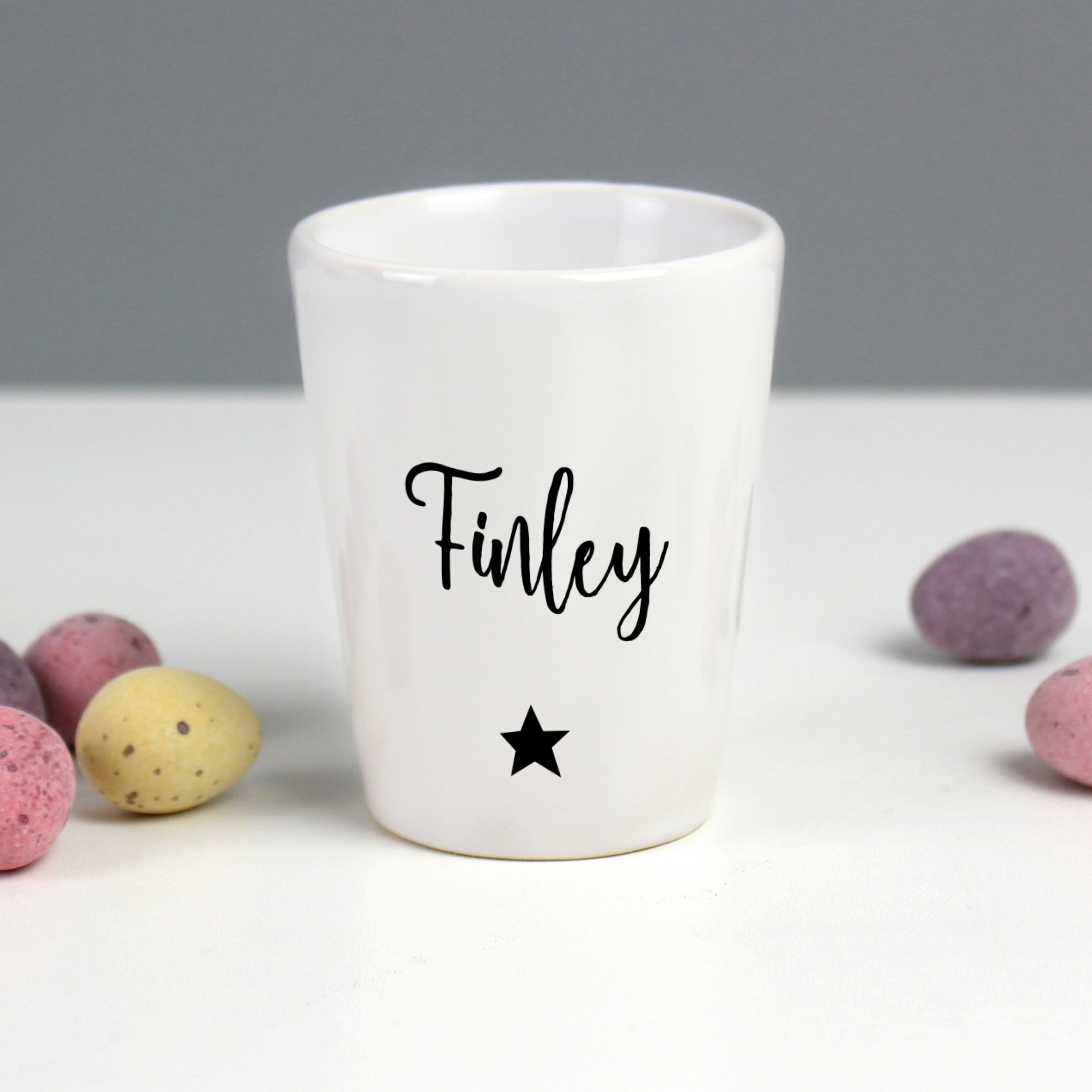 A white ceramic egg cup with the name 'Stanley' printed on it, alongside a spoon and a piece of toast, with an egg placed in the egg cup.