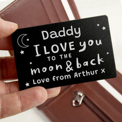 A black wallet card with white text saying 'Daddy I love you to the moon & back - Love from Arthur X', held against a brown wallet background.