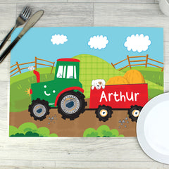 A colourful personalised placemat featuring a tractor design with the name 'Arthur' printed on it, placed on a table with a fork and knife on either side.