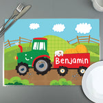 A colourful personalised placemat featuring a tractor design with the name 'Arthur' printed on it, placed on a table with a fork and knife on either side.