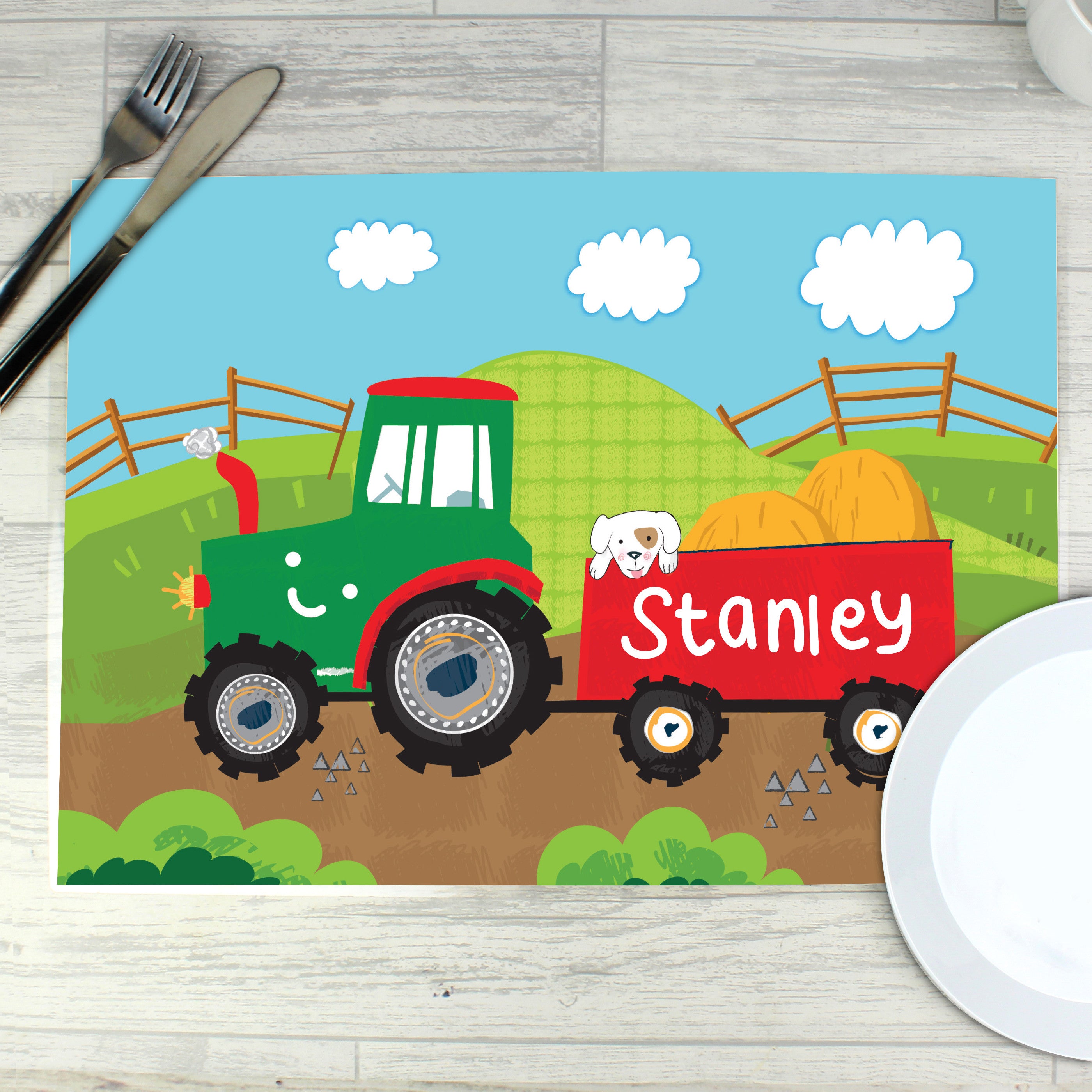 A colourful personalised placemat featuring a tractor design with the name 'Arthur' printed on it, placed on a table with a fork and knife on either side.