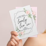 A personalised voucher card with floral design and the text 'This token entitles you to breakfast in bed' along with the name 'Amelia'. The card is displayed on a wooden surface with a round brown plate behind it. 02