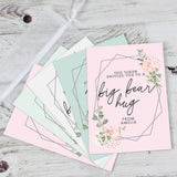 A personalised voucher card with floral design and the text 'This token entitles you to breakfast in bed' along with the name 'Amelia'. The card is displayed on a wooden surface with a round brown plate behind it. 05