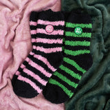 Two pairs of striped socks, one pink and black, one green and black, on a textured surface.
