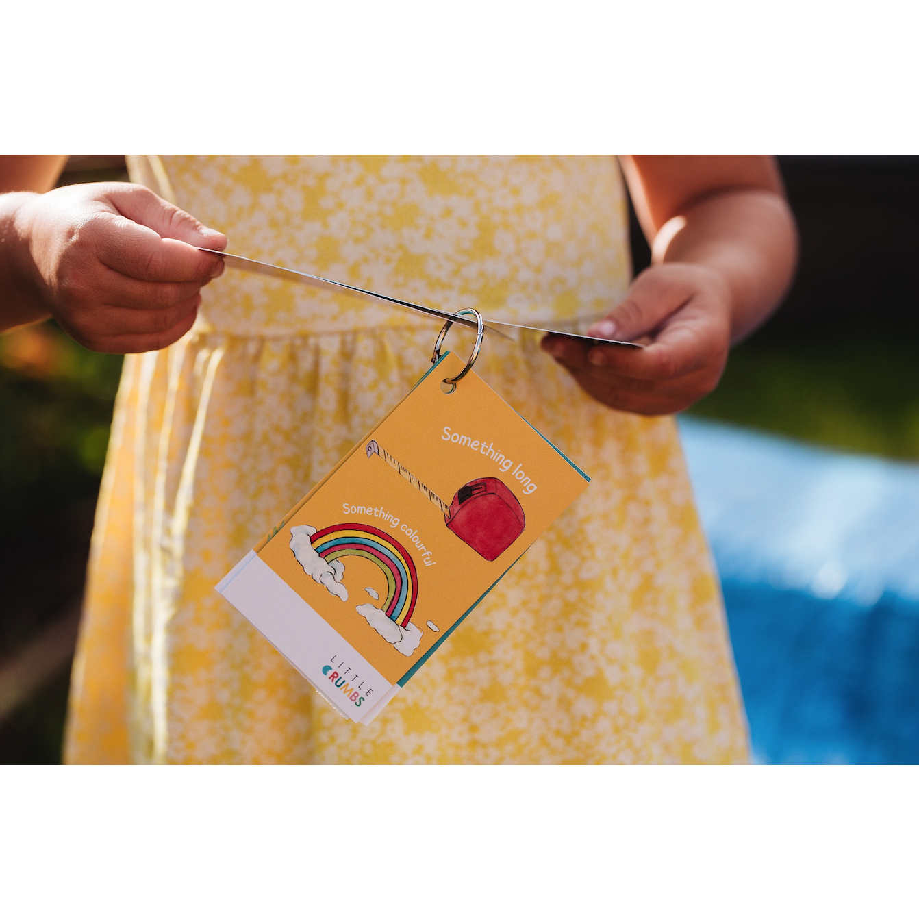 A child holding a scavenger hunt card with a rainbow and a red apple on it, in front of a blue background.