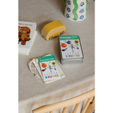 A child holding a scavenger hunt card with a rainbow and a red apple on it, in front of a blue background.