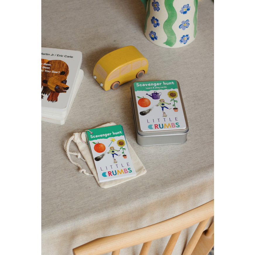 A child holding a scavenger hunt card with a rainbow and a red apple on it, in front of a blue background.