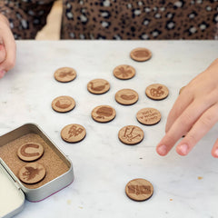 A collection of wooden story tokens with fairytale themed engravings, placed on a marble surface with a person's hand reaching out to pick up a token.