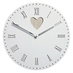 A vintage white wall clock with heart detail displayed on a wall next to a vase with flowers.