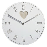 A vintage white wall clock with heart detail displayed on a wall next to a vase with flowers.