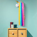 A colourful unicorn wall hanging decoration with a blue background, hanging over a wooden cabinet with a mug and a coffee pot on it.