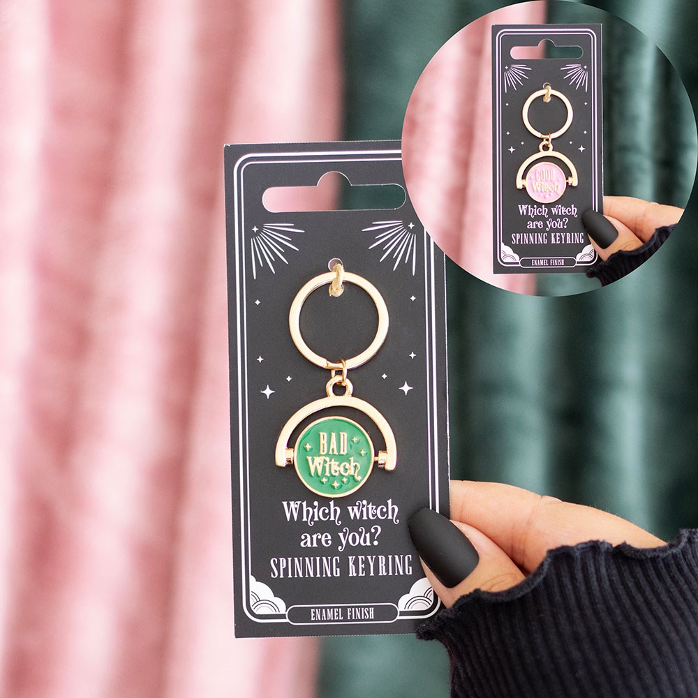 Keyring with 'Bad Witch' design on a black card, held by a hand against a pink curtain.