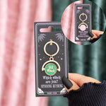 Keyring with 'Bad Witch' design on a black card, held by a hand against a pink curtain.