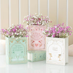 Three decorative planters filled with pink and white flowers, each on top of a book with text.