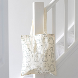 Tote bag with cat pattern hanging on a white railing.