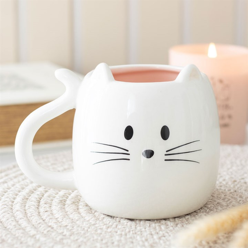 Cat-shaped ceramic mug with a cute face on a textured surface.