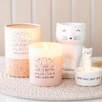 Candle with cat-themed design and decorative cat figurines on a textured surface.