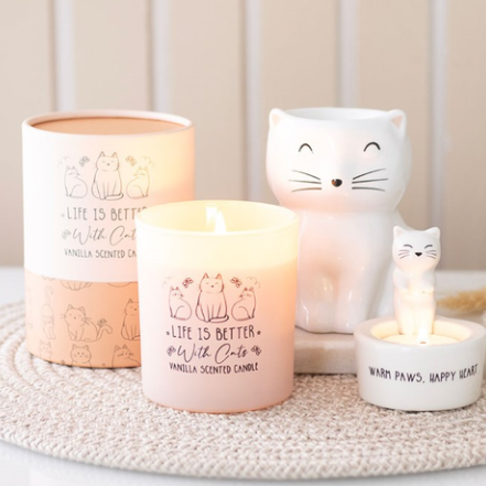 Candle with cat-themed design and decorative cat figurines on a textured surface.