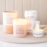 Candle with cat-themed design and decorative cat figurines on a textured surface.