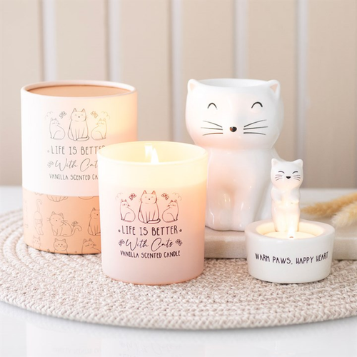 Candle with cat-themed design and decorative cat figurines on a textured surface.