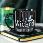 Black mug with 'Wicked Without Coffee' text on a book with a green candle in the background
