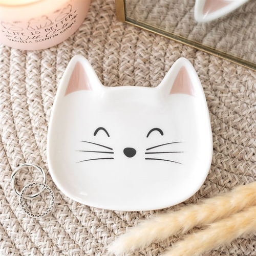 White ceramic dish shaped like a cat face on a textured surface with a candle and mirror in the background.
