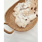 A baby lying on a cream-colored fringe blanket with floral patterns and a visible brand tag on the blanket.